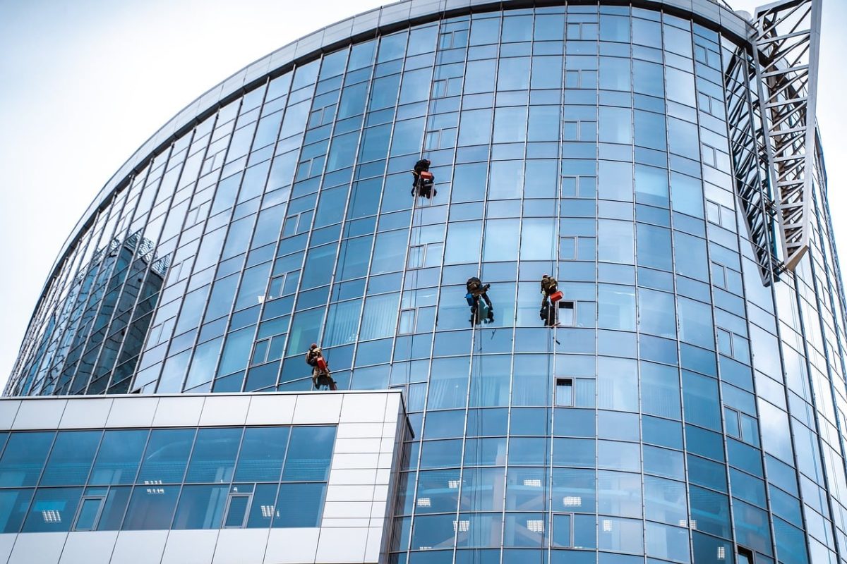 window cleaning, modern architecture, glass building, skyscraper construction, building maintenance, high-rise worker, urban landscape, building facade, urban climbing, safety equipment, rope work, cleanliness, workwear, weather conditions, outdoor work, access systems, tall buildings, architectural design, office building, blue glass