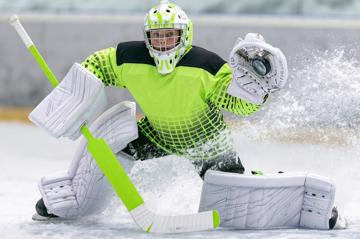 ice hockey, goalie, young athlete, protective gear, hockey stick, puck, ice rink, youth hockey, catching glove, winter sport, dynamics, neon jersey, movement, sporting event, concentration, goalie mask, goalie pads, energy
