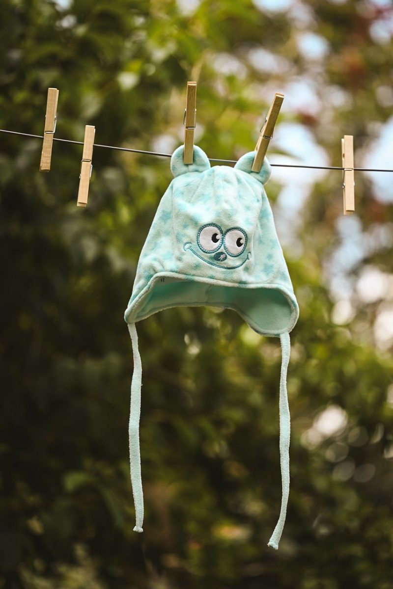 baby hat, cartoon eyes, wooden clothespins, outdoor drying, blue hat, garden setting, cute, baby clothing, hanging on line, baby design, plush fabric, children's textiles, light bokeh, spring theme, felt ears, suspend, clothesline, play area, felt fabric, summer theme