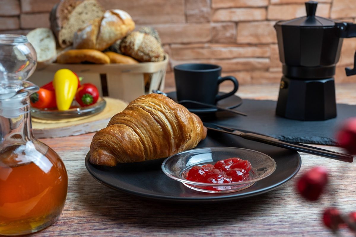breakfast, croissant, jam, honey, coffee machine, coffee pot, black dishes, bread basket, bun, paprika, tomatoes, rustic table, baked goods, morning meal, mediterranean, comfortable, food scene, enjoyment, café atmosphere