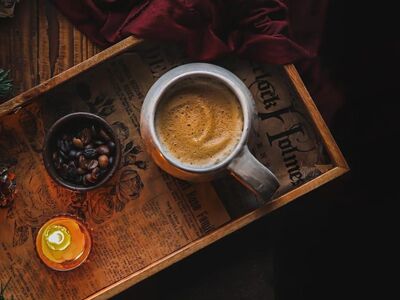 coffee mug, wooden tray, foam art, coffee beans, small bowl, lit candle, candle flame, vintage newspaper, red fabric, pinecone, moody lighting, warm aesthetic, top view, cozy morning, rustic table, caffeine, relaxation, background textures, dark food photography, green branch