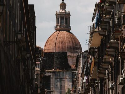 catania, cathedral, city landmark, narrow street, historic architecture, overcast sky, italian cityscape, cobblestone, pedestrians, old buildings, southern italy, travel photography, tourism, urban silhouette, city life, dome, streetscape, local architecture, culture, europe, summer day