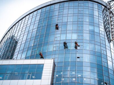 window cleaning, modern architecture, glass building, skyscraper construction, building maintenance, high-rise worker, urban landscape, building facade, urban climbing, safety equipment, rope work, cleanliness, workwear, weather conditions, outdoor work, access systems, tall buildings, architectural design, office building, blue glass