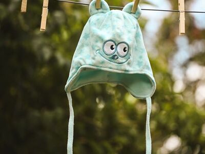 baby hat, cartoon eyes, wooden clothespins, outdoor drying, blue hat, garden setting, cute, baby clothing, hanging on line, baby design, plush fabric, children's textiles, light bokeh, spring theme, felt ears, suspend, clothesline, play area, felt fabric, summer theme