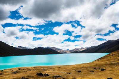 yamdrok lake, tibetan plateau, sacred lake, turquoise water, snow-capped mountains, lakeside shore, alpine grassland, blue sky, cumulus clouds, dramatic landscape, natural landscape, panorama, wild, exploration, tranquil, clean air, mountain region, vacation escape, peaceful atmosphere